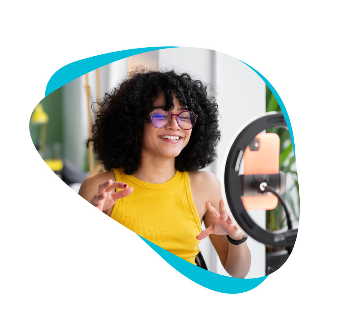 A woman with curly hair recording or streaming video on her smartphone. The smartphone is connected to a ring light.
