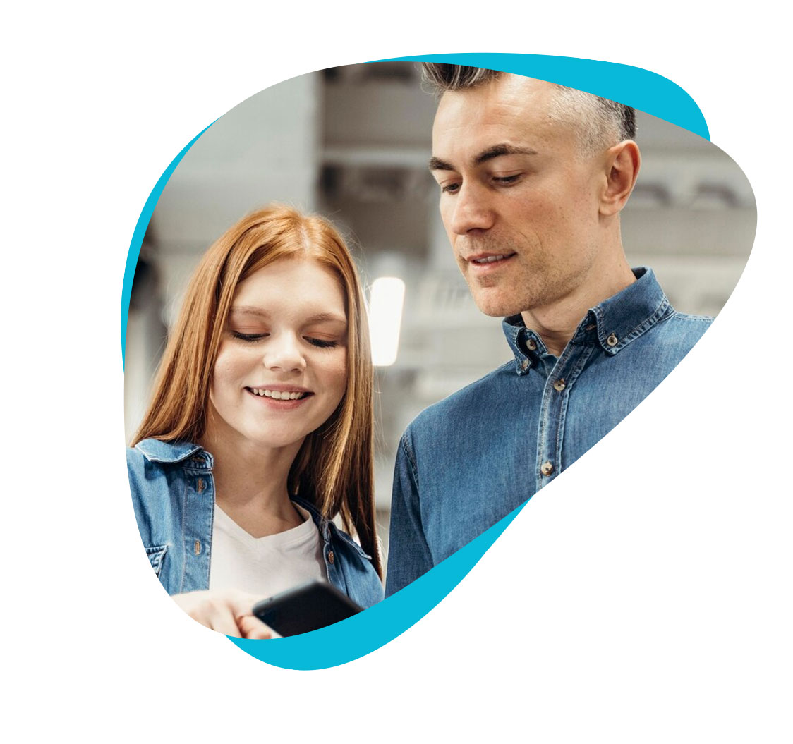 Man and smiling woman wearing denim jackets and looking at a smartphone.